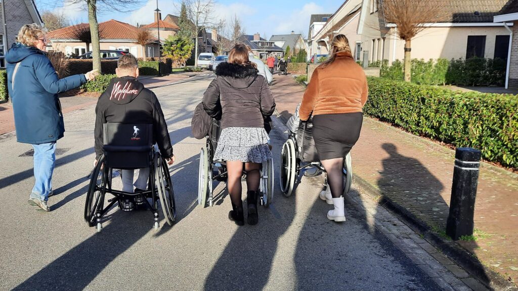 rolstoelgebruikers wandelen samen in een rustige straat met bomen en gebouwen