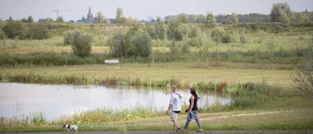 wandelaars met hond langs water in groen landschap